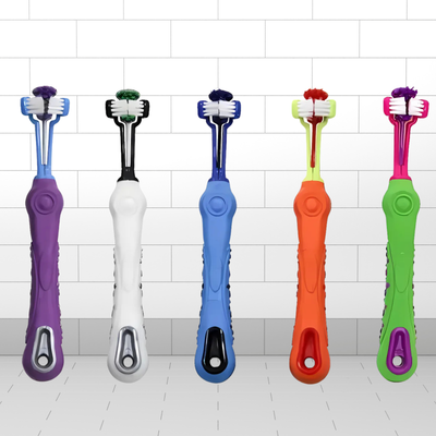 Five colorful toothbrushes for dog with different handles and bristle designs on a tiled bathroom floor.