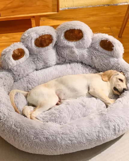Dog lying on a fluffy paw-shaped pet bed with wooden floor in the background