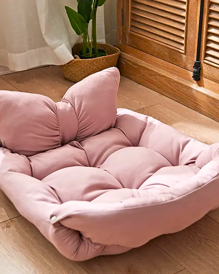 Pink butterfly-shaped cushion on a wooden floor with a plant in the background