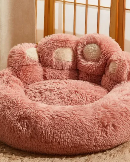Pink paw-shaped pet bed on a carpeted floor with a neutral-colored wall in the background.