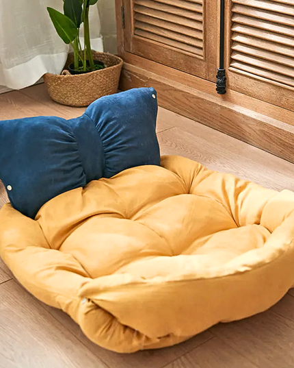 Yellow pet bed with a blue pillow on a wooden floor