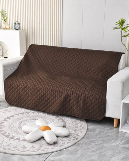 Brown quilted sofa cover on a white sofa in a living room setting.