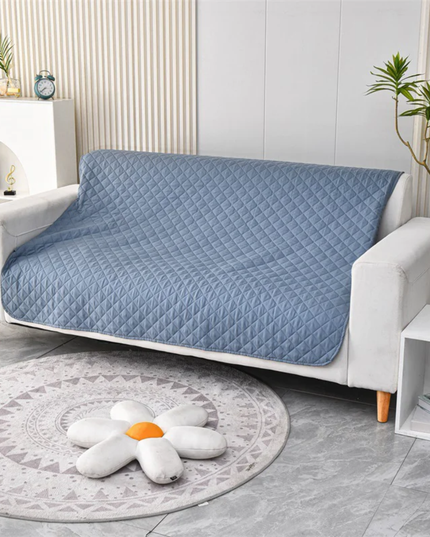 Blue quilted sofa cover on a white sofa in a living room setting.
