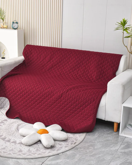 Red quilted blanket draped over a white sofa in a living room setting.
