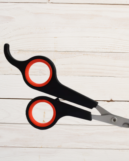 Black and red pet nail clippers on a light wooden surface