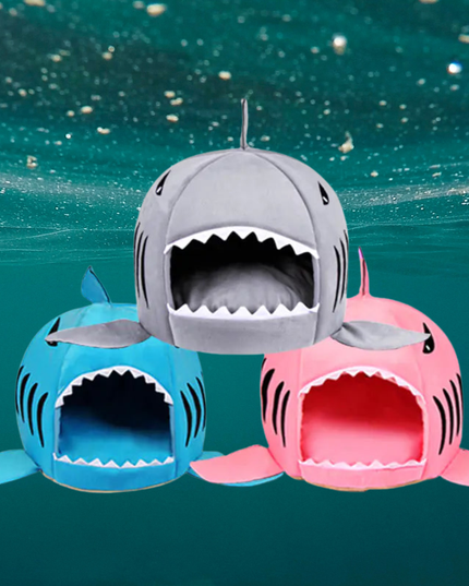 Three shark-shaped pet beds in gray, blue, and pink on a teal underwater background.