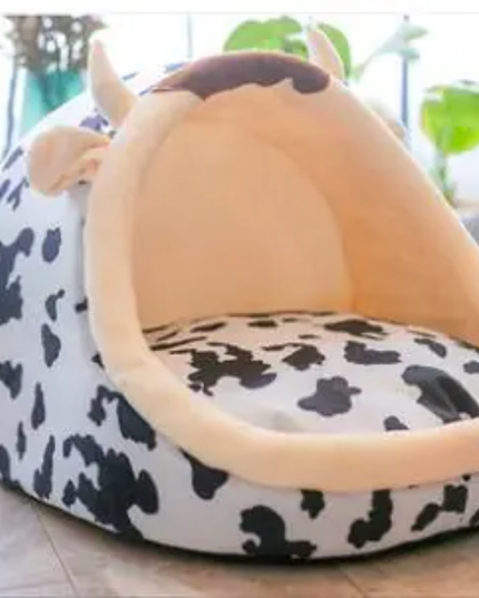 Cow-patterned pet bed with a beige interior on a light wooden floor.