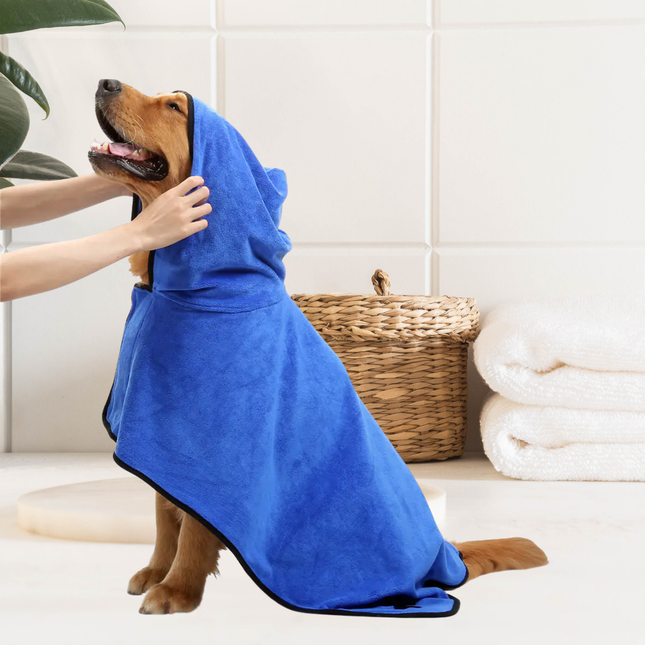 Dog wearing a blue towel with a person assisting, in a bathroom setting.