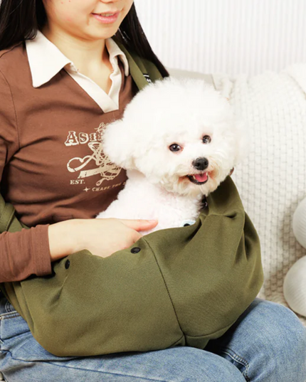 Person holding a small white dog in a green pet sling on a couch.