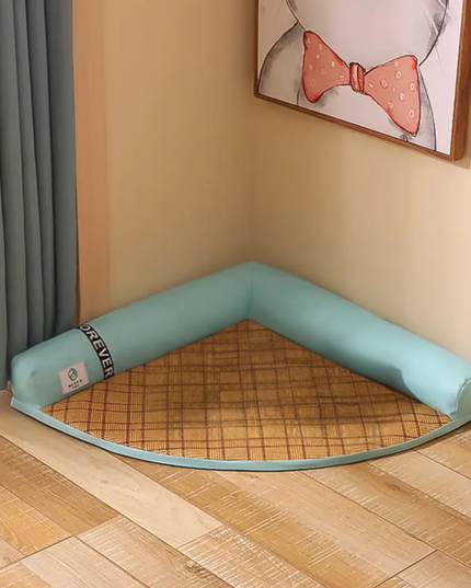 Corner pet bed with a checkered mat on a wooden floor, framed picture on the wall.