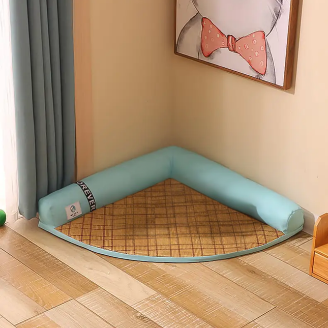 Corner pet bed with a checkered mat on a wooden floor, framed picture on the wall.