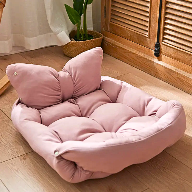 Pink butterfly-shaped cushion on a wooden floor with a plant in the background