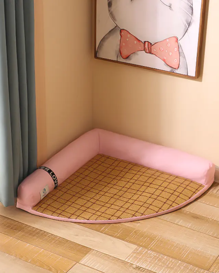 Pet bed with pink cushion on a wooden floor, framed picture of a cat in the background.