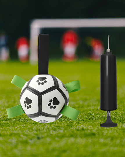 Soccer ball with green straps and black pump on grass with blurred goalposts in the background
