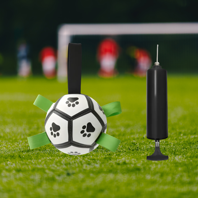 Soccer ball with green straps and black pump on grass with blurred goalposts in the background