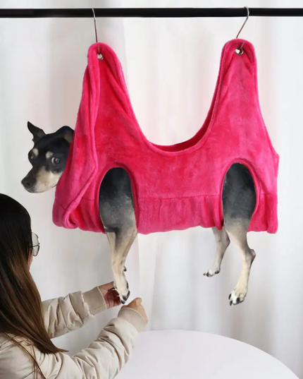 Dog wearing a pink tank top hanging from a hook, with a person looking at it.
