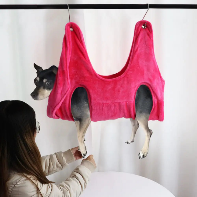 Dog wearing a pink tank top hanging from a hook, with a person looking at it.