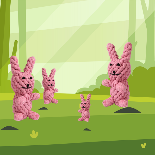 Four pink knitted bunnies in a forest setting with green trees and grass.