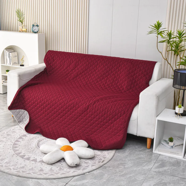 Red quilted blanket draped over a white sofa in a living room setting.
