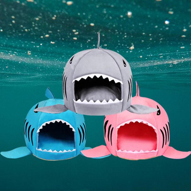 Three shark-shaped pet beds in gray, blue, and pink on a teal underwater background.